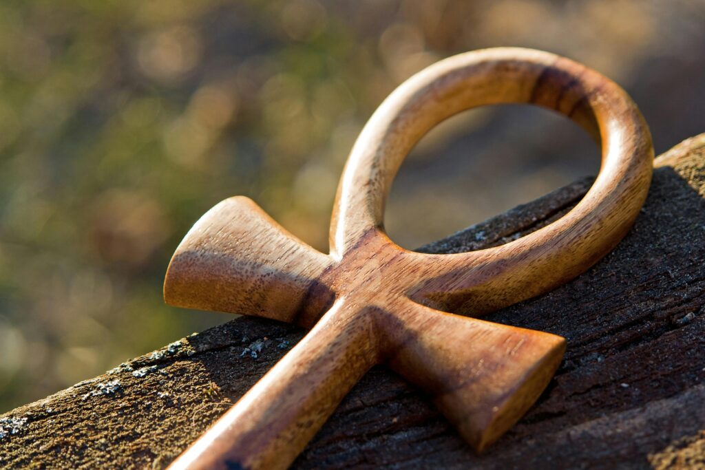 ank-cross-spiritual-egypt-161147-161147 Detailed view of a wooden ankh symbol resting on a tree trunk, emphasizing its spiritual and historical significance.