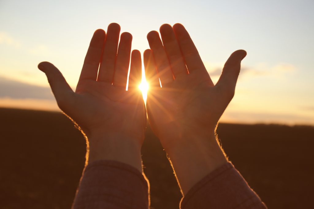 Hands of religious man praying outdoors at sunset